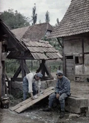 Två franska soldater tar hand om sin tvätt med hjälp av brädor som satts upp på tråget till en fontän nära en bondgård i staden Gildwiller, departement Haut-Rhin, Alsace, Frankrike, 21 juni 1917 (a